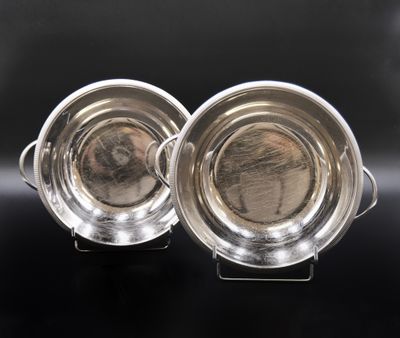 deux plats en métal argenté posés sur des supports, sur un fond noir