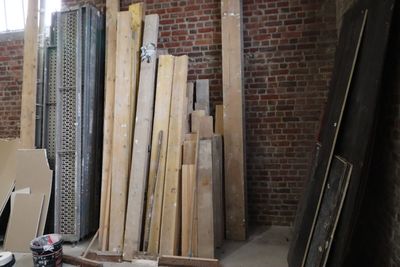 Plusieurs morceaux de bois sont empilés dans une pièce dont le mur est en briques.
