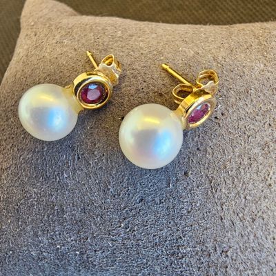 une paire de boucles d'oreilles en perles et rubis posée sur un coussin