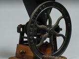 un moulin à café à l'ancienne posé sur un socle en bois, sur fond gris