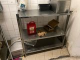 an image of a kitchen with a metal shelf and a trash can