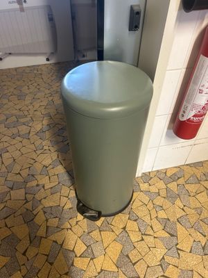 a green trash can sitting on the floor in a bathroom