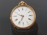 a small gold pocket watch sitting on top of a black stand