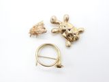 two gold turtle brooches and a gold ring on a white surface