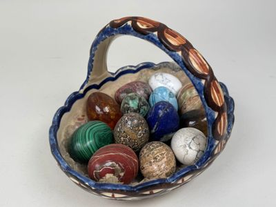 un panier rempli de pierres de différentes couleurs posé sur une surface blanche