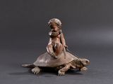 bronze figurine of a child on a turtle on a black background