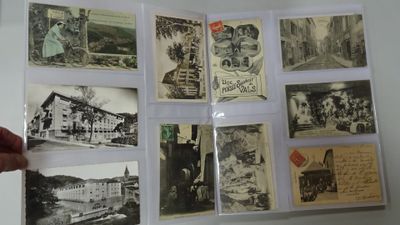 a person holding a pair of scissors in front of a bunch of old postcards