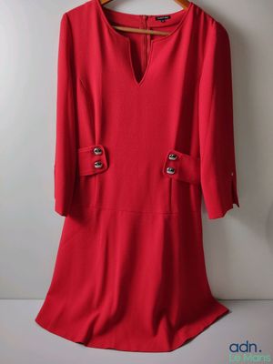 une robe rouge suspendue à un cintre devant un mur blanc