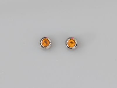 une paire de boucles d'oreilles en saphir orange posées sur une surface blanche