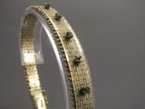 un gros plan sur un bracelet en or orné de pierres vertes