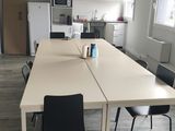 une longue table au milieu d'une pièce, avec des chaises et un réfrigérateur