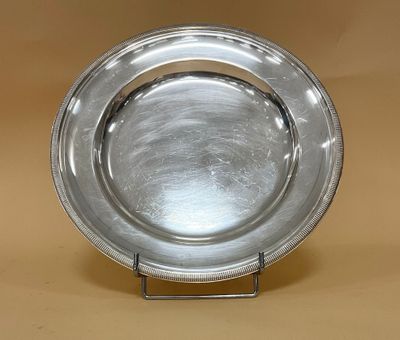 une assiette en argent posée sur un support métallique, sur un fond beige clair