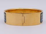 a close up of a gold bracelet with a blue stone in the center
