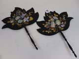 deux épingles à cheveux noires ornées de fleurs et de feuilles, posées sur une table