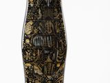 un vase noir et doré posé à côté d'une feuille verte