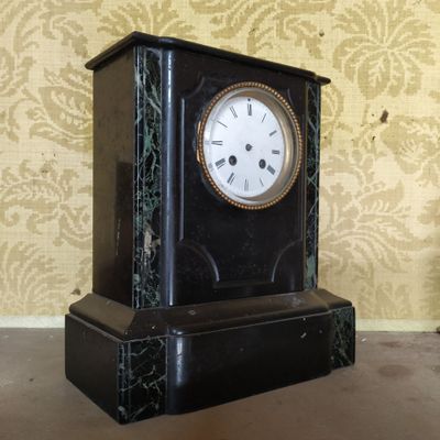 une horloge noire posée par terre devant un mur