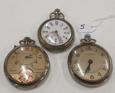 Trois montres de poche anciennes sont exposées sur un support blanc