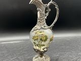 un vase ancien en métal argenté, orné de fleurs, posé sur une table