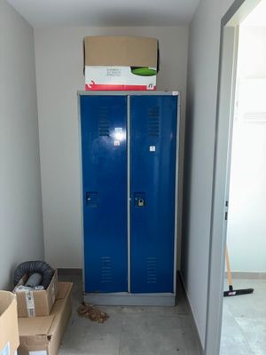 un casier bleu dans une pièce où s'entassent des cartons, les uns sur les autres, par terre