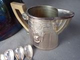 a silver pitcher with spoons next to it on a table