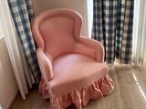 a pink chair sitting in front of a window next to a curtain