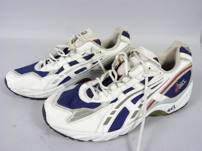 pair of white and blue sneakers on a white surface with a glass of wine in the background