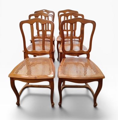 four wooden chairs with cane backrests are lined up against a white background