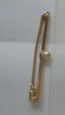 une broche en or ornée d'une perle, posée sur un morceau de papier