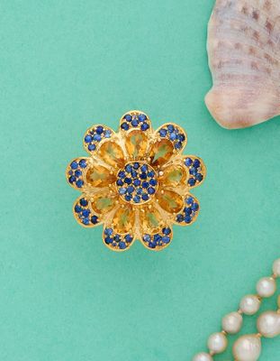 broche représentant une fleur dorée et bleue ornée de perles sur fond turquoise