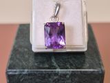 une photo d'un pendentif en pierre violette posé sur une boîte blanche