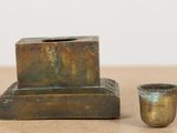 a small cup sitting next to a small bronze candle holder