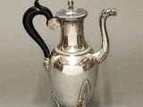 an antique silver tea pot with a black handle sitting on a table