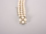 a close up of a white pearl bracelet with a diamond clasp