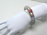 une main de mannequin blanche tenant une bague sertie d'une pierre rouge