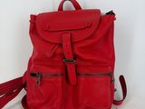 un sac à dos en cuir rouge auquel est accrochée un pompon