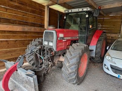un tracteur rouge garé dans un garage à côté d'une voiture argentée