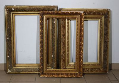 trois cadres dorés posés sur un sol carrelé, près d'un mur
