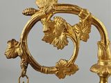 a gold clock on a stand with a red jewel
