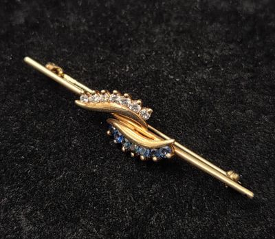 un gros plan d'une broche en or ornée de pierres bleues et blanches
