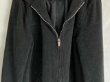 black jacket with hood and zippers hanging on a hanger on a wall