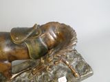 bronze statue of a man laying down with his head on a horse