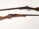 On voit deux armes à feu posées sur une surface blanche, avec un fond blanc.