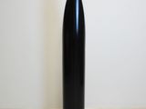 a black vase sitting on the floor next to a white wall