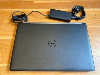 un ordinateur portable Dell avec son chargeur et son cordon d'alimentation posé sur une table en bois