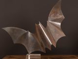 sculpture représentant une chauve-souris posée sur une table en bois devant un mur noir