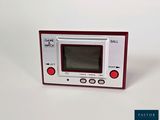 une console Game & Watch rouge et blanche posée sur une surface blanche