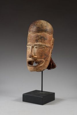 un masque en bois posé sur un socle noir, sur fond gris