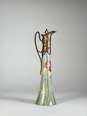 un vase en verre muni d'une poignée en métal posé sur une surface blanche