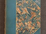un vieux livre posé sur une table recouverte d'un tissu bleu et or