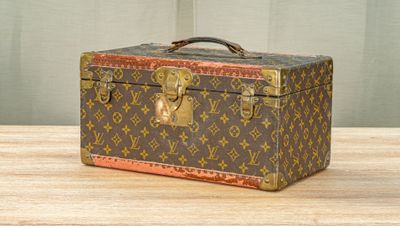 Une malle Louis Vuitton posée sur une table en bois, sur fond vert